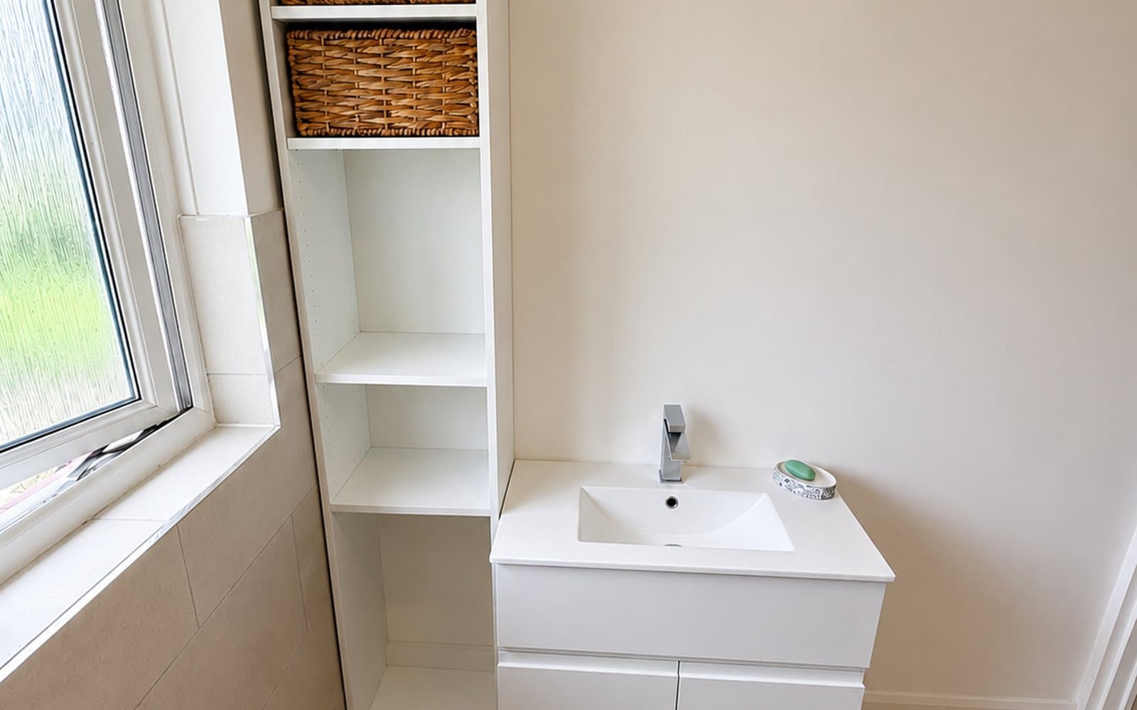Wall-hung vanity unit with basin beside a tall open shelving tower under a frosted window